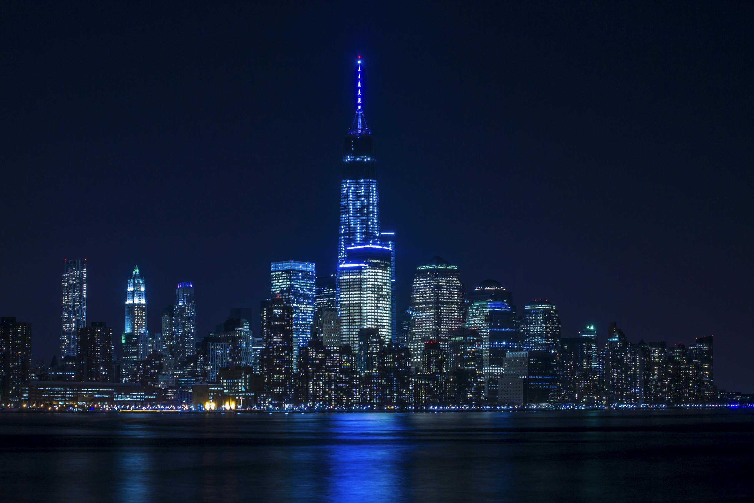 Illuminated New York City skyline reflecting over the Hudson River at night.