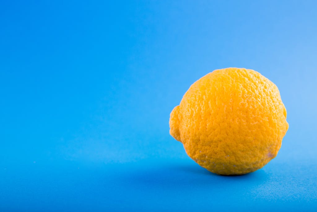 Vivid close-up of a ripe lemon against a bright blue background, emphasizing freshness.